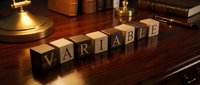 Wooden letter blocks spelling VARIABLE on polished desk with vintage brass lamp and books in warm office setting for business concepts.