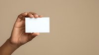 Hand of a man with medium brown skin tone holding a blank white business card against a neutral beige background. Suitable for branding, corporate identity, and marketing materials.
