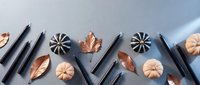 Autumn flat lay with black pencils, copper metallic leaves and decorative pumpkins arranged on gradient background for seasonal creative projects.