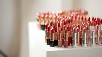 Professional makeup collection featuring rows of luxury lipsticks in various shades from nude to deep red arranged on white display shelves.