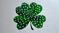 Green four-leaf clover with white polka dots painted on textured paper, symbol of luck and Irish tradition for St. Patrick's Day celebrations.