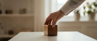 Hand placing wooden cube block on white table in bright modern interior for business concept and strategic planning.