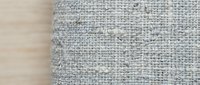 Natural linen burlap fabric texture with frayed edges on wooden surface for rustic crafting and home decor projects.