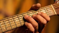 Close-up of male musician fingers pressing guitar strings on fretboard during performance. Warm lighting highlights hand position and musical technique.