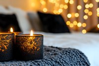 Glowing candles in decorative holders on knitted blanket with warm bokeh lights background create cozy winter atmosphere for holiday season and home decor.