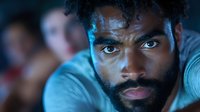 Close up portrait of young African American man with beard and intense gaze looking directly at camera in dramatic blue lighting, expressing determination and strength.