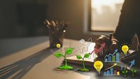 Business growth concept with plant sprouting from coins, financial charts, lightbulb ideas and upward arrows on office desk representing investment success.
