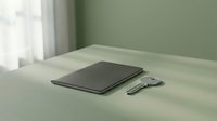 Closed laptop and keys on minimal desk with sage green wall and natural light from window, workspace setup.