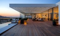 Luxury penthouse terrace with wooden deck, modern furniture and decorative ceiling pattern, illuminated at sunset overlooking city skyline and mountains.