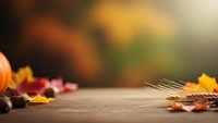 Autumn leaves scattered on wooden surface with warm bokeh background creating cozy seasonal atmosphere for fall decorating and harvest themes.