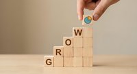 Hand placing wooden block with growth chart icon on GROW word blocks arranged as ascending stairs representing business development and progress concept.