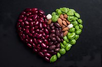 Heart shape made from colorful beans and nuts on black background, including red kidney beans, black beans, almonds and green peas arranged in creative pattern.