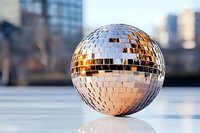 Shiny disco ball with mirror tiles reflecting golden light on white surface against blurred urban cityscape background for party and entertainment concepts.