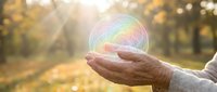 Elderly hands gently holding glowing rainbow sphere in autumn park with golden sunlight rays creating magical atmosphere for wellness and spiritual concepts.