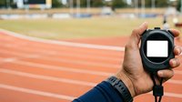 Close-up of hand holding sports stopwatch on running track. Coach or athlete timing performance during training session at outdoor stadium with blurred background.