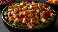 Juicy grilled chicken pieces with colorful bell peppers and fresh greens on black plate, glazed in sweet and savory Asian-style sauce, served on bed of lettuce.