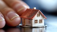 Hand protecting miniature house model symbolizing home insurance, real estate investment security and property protection concept.