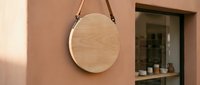 Modern round wooden mirror with leather strap hanging on terracotta wall next to window, minimalist Scandinavian home decor interior design element.