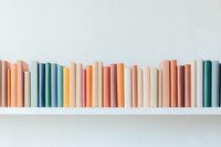 Row of books in pastel colors arranged on white shelf against light wall, creating minimal contemporary aesthetic for home decor and library design.
