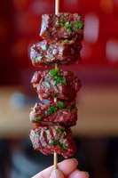 Raw marinated beef chunks on wooden skewer garnished with fresh herbs and spices against blurred red background. Close up of meat kebab appetizer.