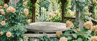 Empty wooden round table in garden with blooming roses and climbing vines, suitable for outdoor dining, product display, or garden design projects.