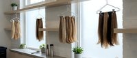 Hair extensions hanging on wooden hangers in modern salon interior with natural lighting and minimalist design for beauty business.