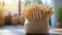 Golden wheat stalks bundled in rustic burlap sack on wooden surface with warm sunlight streaming through window creating cozy farmhouse atmosphere.