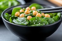 Fresh spinach salad with chickpeas and sesame seeds in black ceramic bowl, served with chopsticks. Healthy vegan meal with protein and greens.