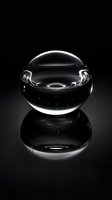 Crystal clear glass sphere with water droplets on black reflective surface, dramatic lighting creates ethereal glow and mirror reflection in minimalist composition.