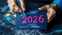 Asian businessman writing 2026 with pink chalk on dark paper, planning future goals and business strategy with colorful sticky notes on textured surface.