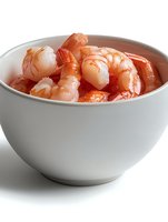 Fresh cooked shrimp served in white ceramic bowl on white background. Closeup of pink prawns showing texture and detail for seafood menu or recipe.