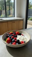 Creamy yogurt bowl topped with fresh strawberries, blueberries, raspberries and blackberries in modern kitchen with natural light and garden views.
