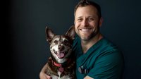 Happy veterinarian in scrubs holding smiling dog patient in clinic. Professional pet healthcare and animal medical treatment concept for veterinary services.