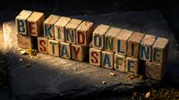 Wooden letter blocks spelling BE KIND ONLINE STAY SAFE message on dark textured surface with dramatic lighting for digital wellness campaigns.