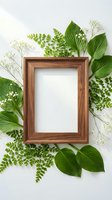 Wooden frame surrounded by fresh green leaves, ferns, and white baby's breath flowers on white background, ideal for spring designs and botanical presentations.