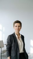 Confident middle-aged Caucasian businesswoman in gray suit standing in modern office environment with natural lighting for corporate presentations.