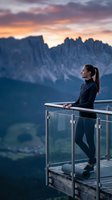 Woman in athletic wear standing on mountain overlook platform gazing at dramatic alpine peaks at sunset, conveying contemplation and adventure for travel and wellness marketing.