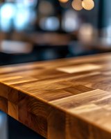 Close-up of butcher block wooden countertop with natural grain pattern and warm tones, blurred bokeh background creates depth and ambiance in kitchen setting.