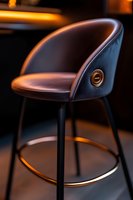 Modern bar stool with curved leather seat and metal frame illuminated by warm ambient lighting in luxurious restaurant or lounge setting.