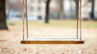 Empty wooden swing with rope hanging in park on blurred natural background, nostalgic childhood memories concept for social media and blogs.