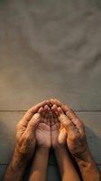 Elderly hands protectively cupping young child hands in prayer gesture on wooden surface symbolizing care, protection, guidance and family bonds.