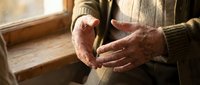 Elderly man's wrinkled hands gesturing during conversation near a window, conveying wisdom, aging, and human connection in warm natural light.
