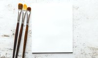 Clean white canvas mockup with three professional paintbrushes on rustic wooden surface, ready for artistic presentation and design projects.