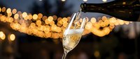 Champagne being poured into a glass against blurred golden bokeh lights, suitable for celebration and luxury event marketing.