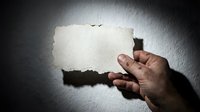 Hand holding blank torn paper sheet against textured wall with dramatic lighting for mockup design projects and creative presentations.