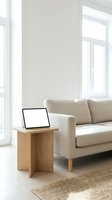 Modern minimalist living room with beige sofa, wooden side table, laptop computer and natural light from large windows for home office workspace design.