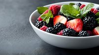 Fresh mixed berries with mint leaves in white ceramic bowl on dark background, healthy organic summer dessert for natural food photography and menu design.