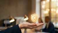 Businessperson holding glowing shield icon representing data protection, cybersecurity, and digital safety in modern office environment for security solutions and risk management concepts.