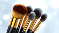 Professional makeup brushes with golden and black handles arranged in diagonal composition against soft bokeh background for cosmetic and beauty industry.