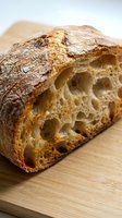 Freshly baked artisan sourdough loaf with crispy crust and open crumb structure on wooden board, ideal for bakery, food, and culinary content.